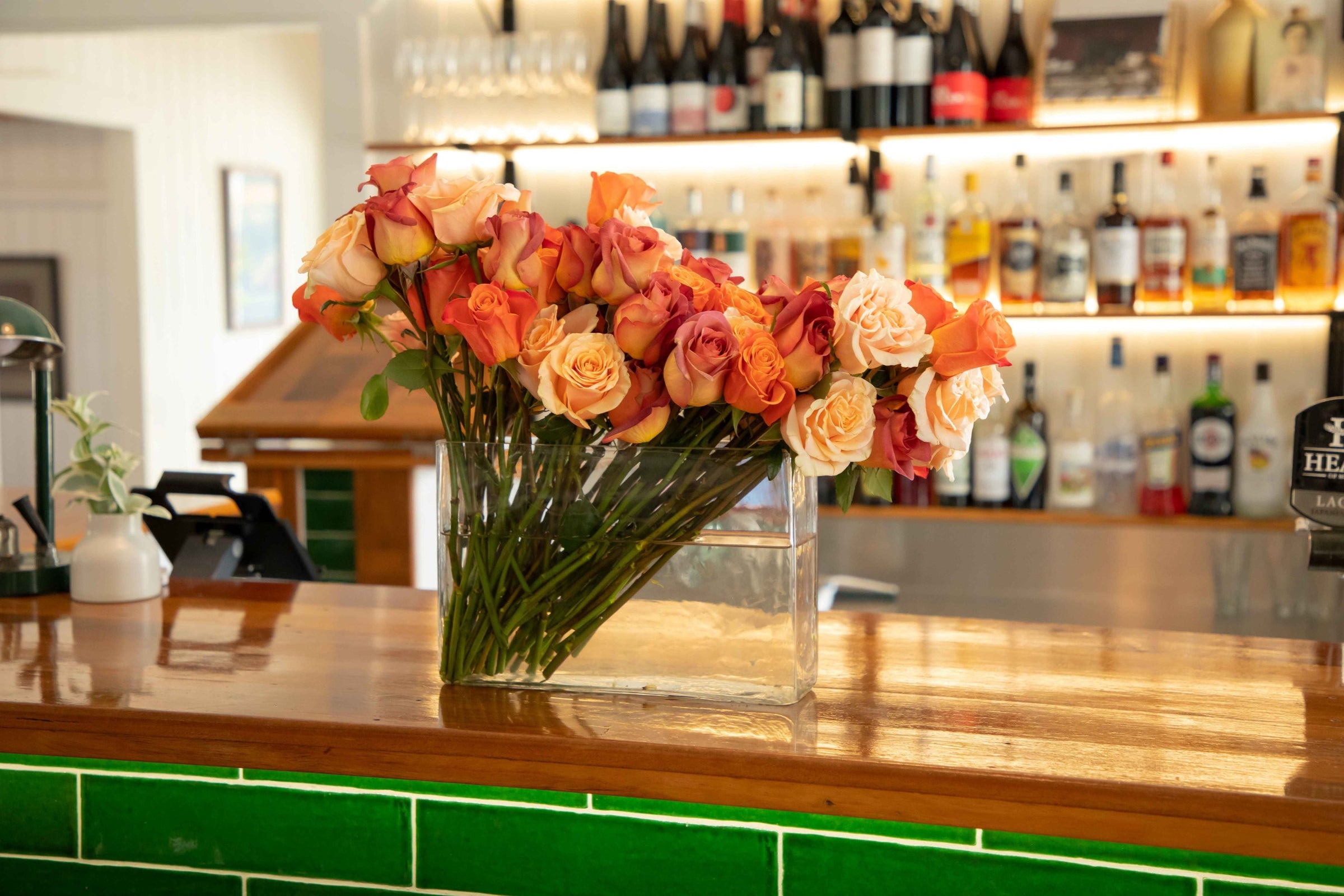 multi-coloured roses placed in hedge style glass vase on timber bar with emerald green tiles under