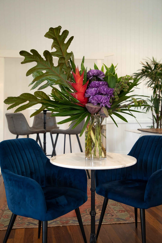 Large vase arrangement filled with unique flowers and foliage fig leaves, grab claws lotus pods and purple Chrysanthemum