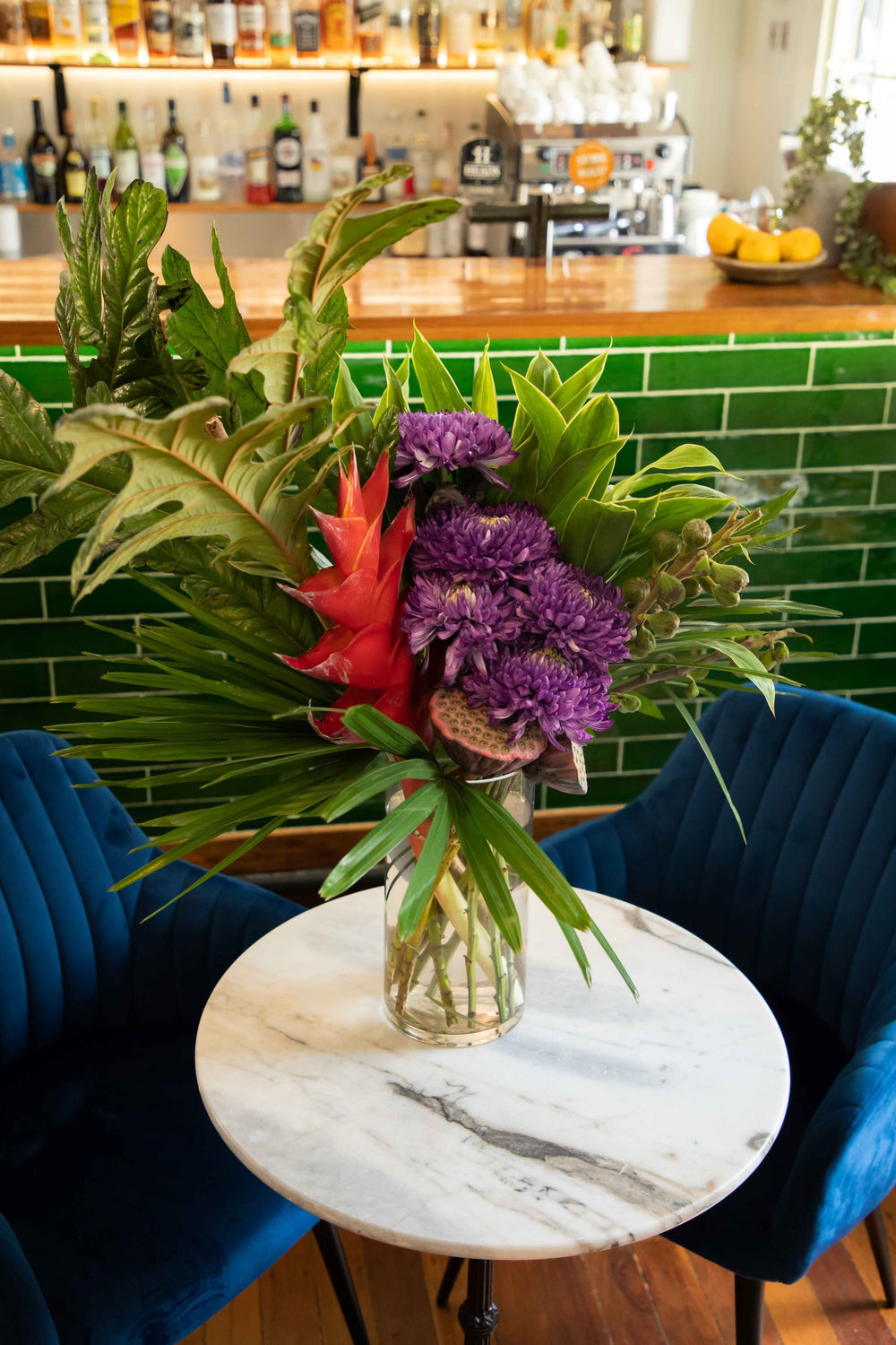 Large vase arrangement filled with unique flowers and foliage fig leaves, grab claws lotus pods and purple Chrysanthemum